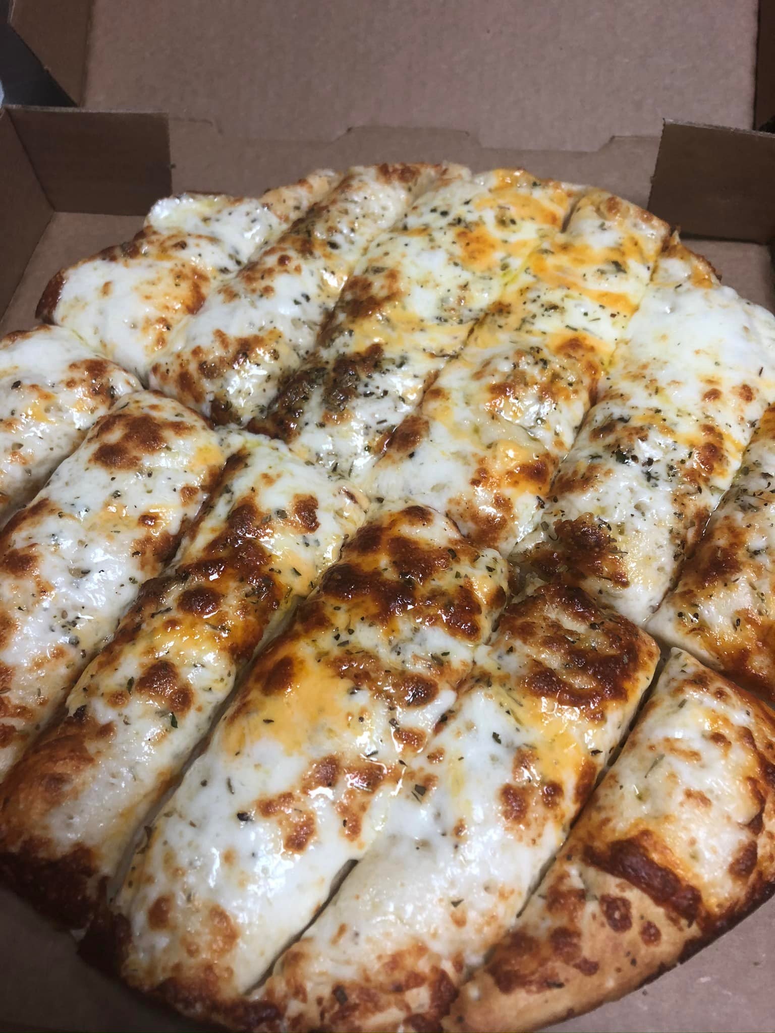 Cheesy breadsticks in a pizza box from Studebakers Pizza & Tap Wall Gatesville TX, topped with melted mozzarella and cheddar cheese, sprinkled with herbs, and cut into rectangular strips.