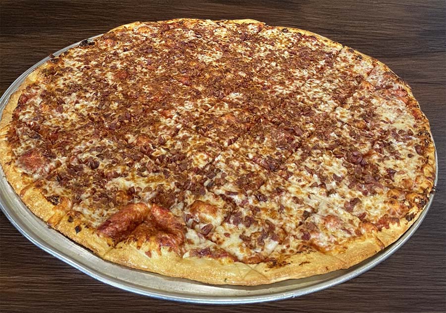 A large, round pizza topped with crumbled bacon and melted cheese, served on a metal tray with a wooden table background at Studebakers Pizza & Tap Wall Gatesville TX.