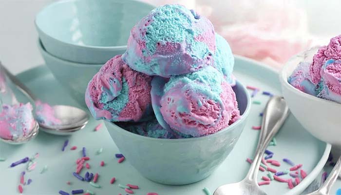 A bowl of blue and pink ice cream scoops sits on a plate with pastel sprinkles, surrounded by empty pastel bowls and silver spoons—perfect for enjoying after pizza, wings, or pasta at Studebakers Pizza & Tap Wall Gatesville TX.