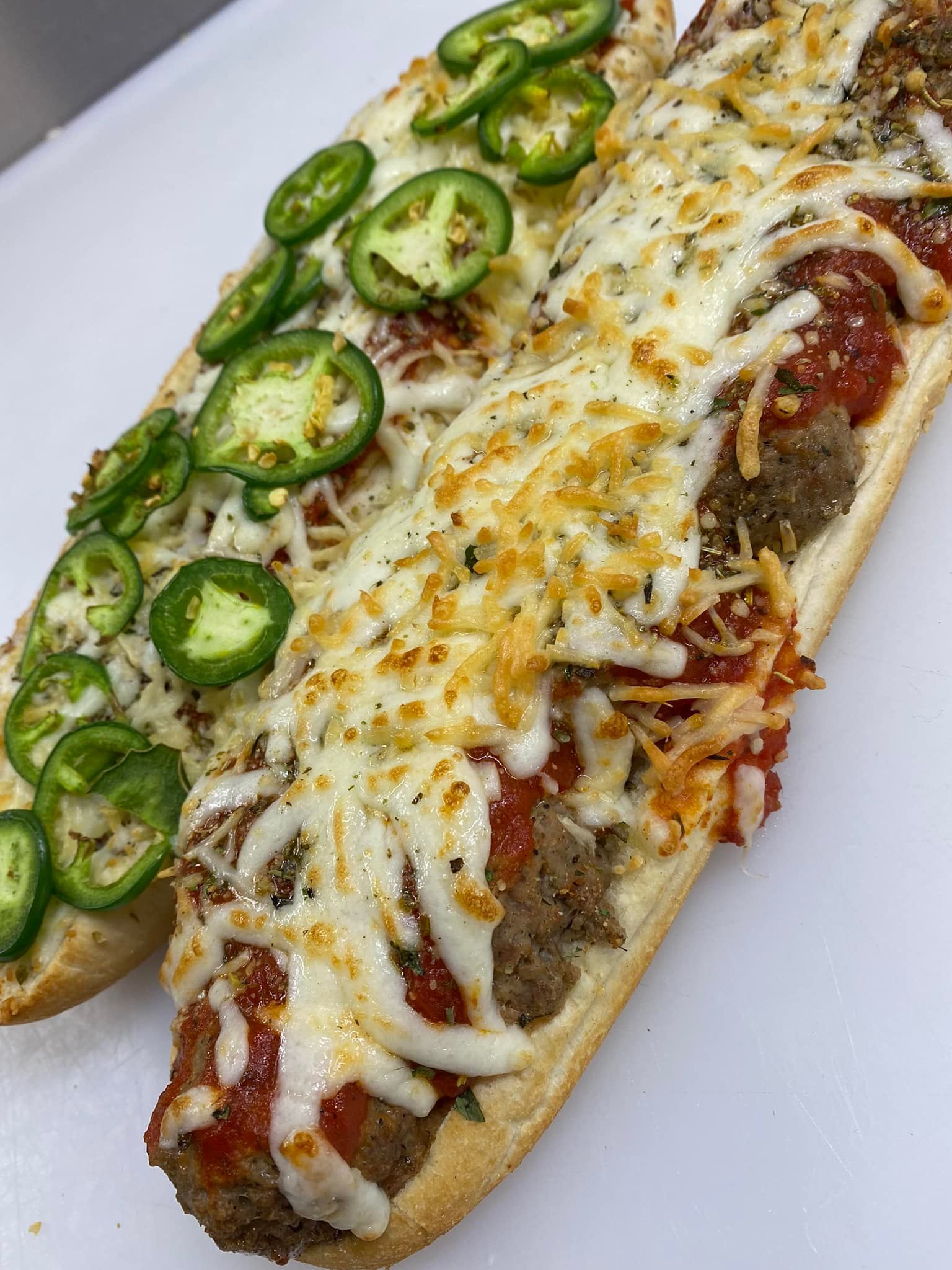 Two toasted open-faced sandwiches from Studebakers Pizza & Tap Wall Gatesville TX, topped with melted cheese, marinara sauce, and meatballs. One features fresh jalapeños, the other just cheese and sauce—both served on a white surface.
