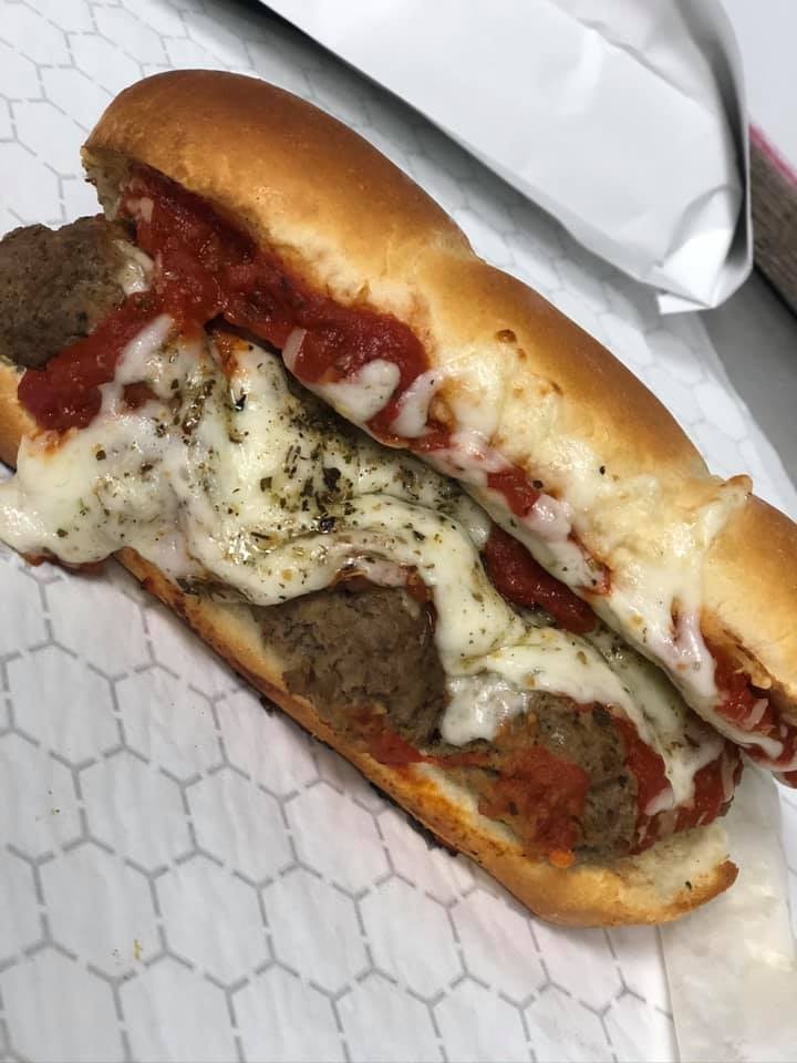A meatball sub on a toasted hoagie roll, topped with melted mozzarella cheese, marinara sauce, and Italian herbs, served fresh at Studebakers Pizza & Tap Wall Gatesville TX, resting on white patterned paper.