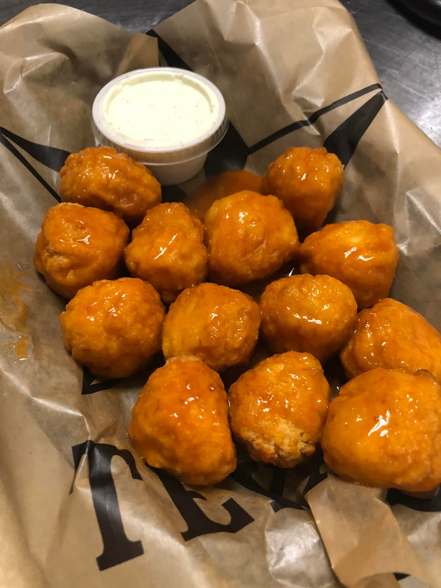 Buffalo-style boneless chicken wings coated in orange sauce are arranged on brown parchment paper at Studebakers Pizza & Tap Wall Gatesville TX, served with a small cup of creamy ranch or blue cheese dip.