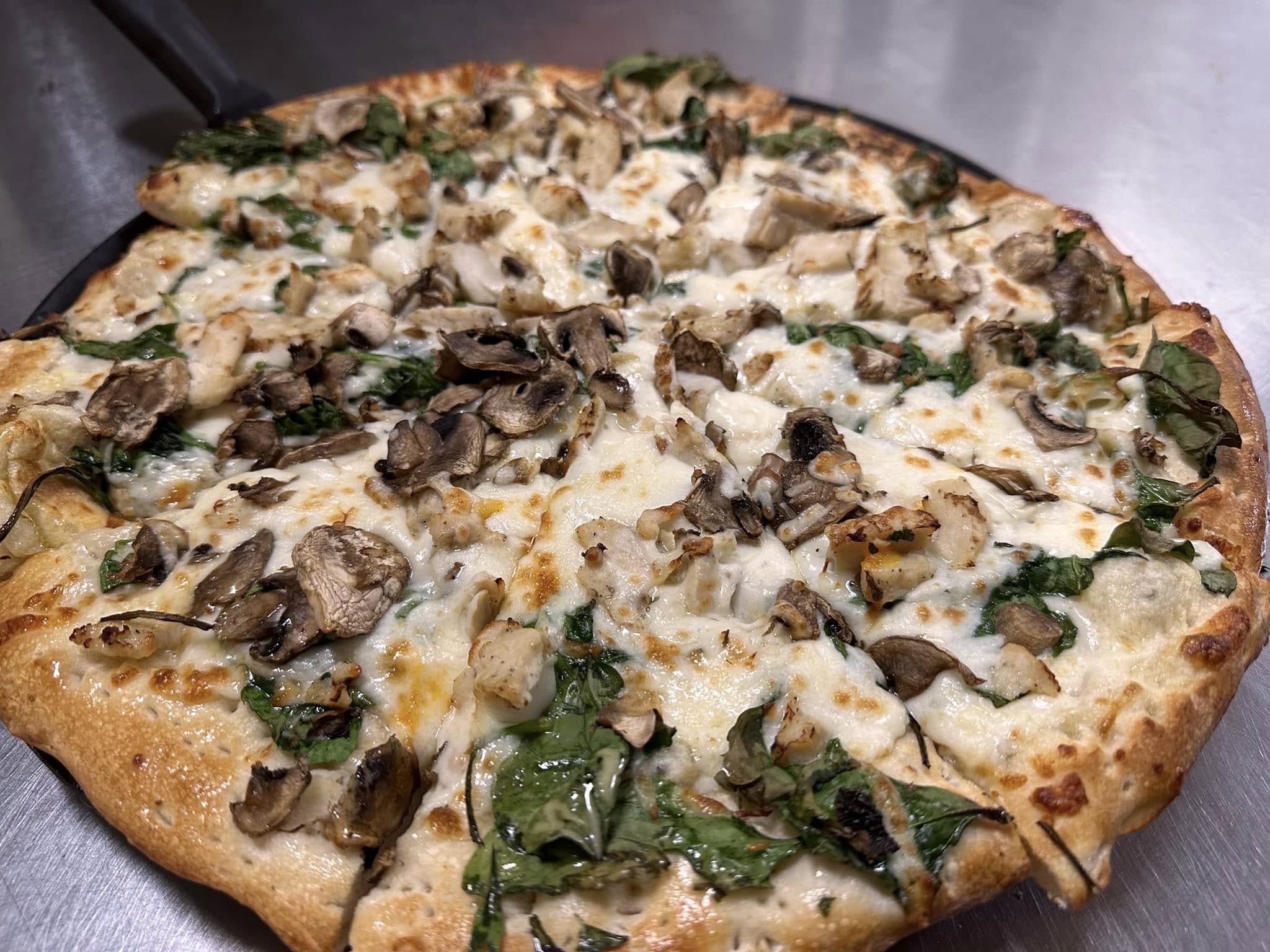 A freshly baked Gatesville Pizza topped with melted cheese, sliced mushrooms, spinach, and pieces of chicken on a golden-brown crust, served hot on a metal tray at your favorite Gatesville Restaurant.