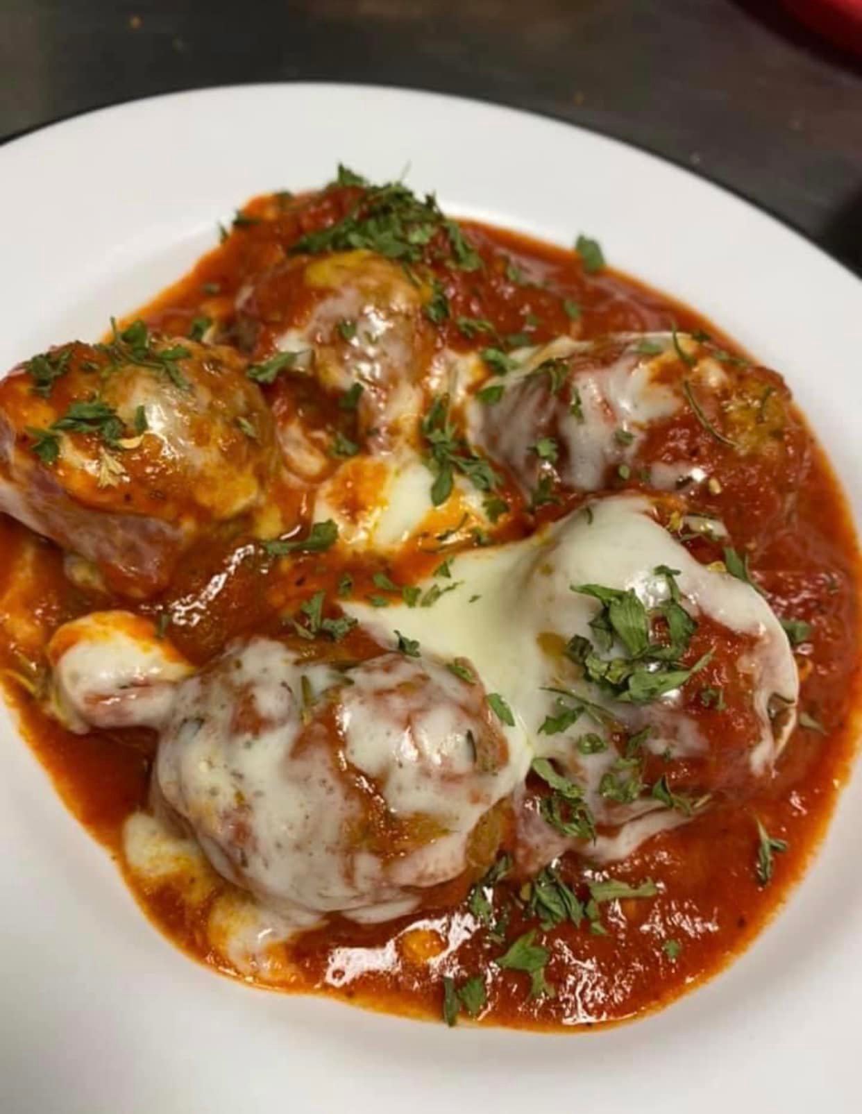 Five meatballs topped with melted cheese and chopped herbs, served on a white plate with tomato sauce—perfect for sharing at Studebakers Pizza & Tap Wall Gatesville TX.