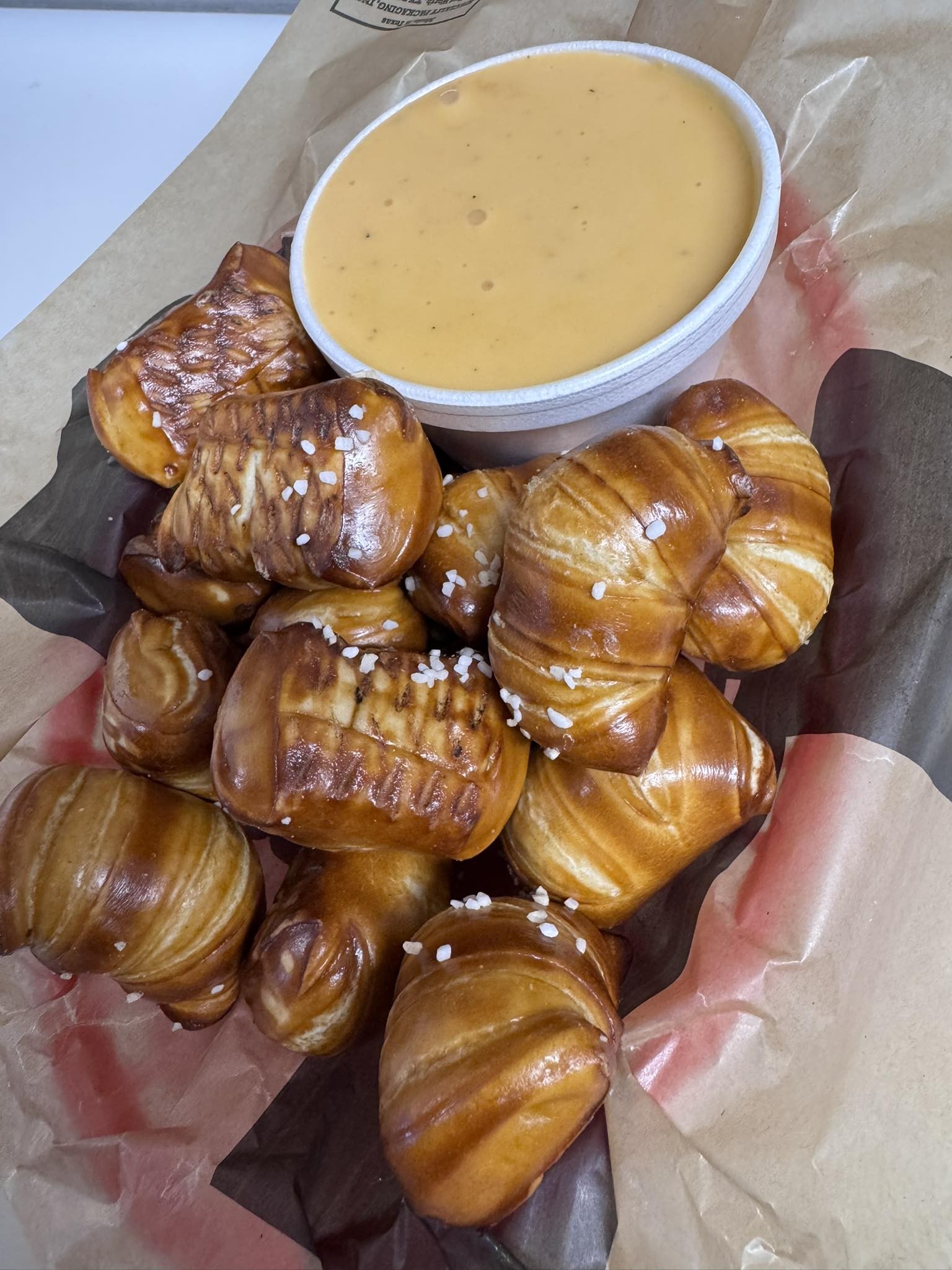 A basket of soft pretzel bites topped with coarse salt, served with creamy cheese dip on brown parchment paper—a perfect snack at Studebakers Pizza & Tap Wall Gatesville TX.