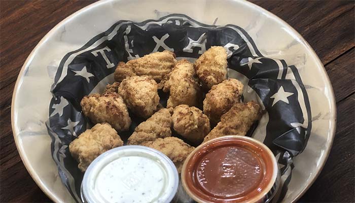 A bowl lined with black and white Texas-themed paper holds several fried pickles, served with ranch and a spicy red sauce—an irresistible snack at Studebakers Pizza & Tap Wall Gatesville TX.