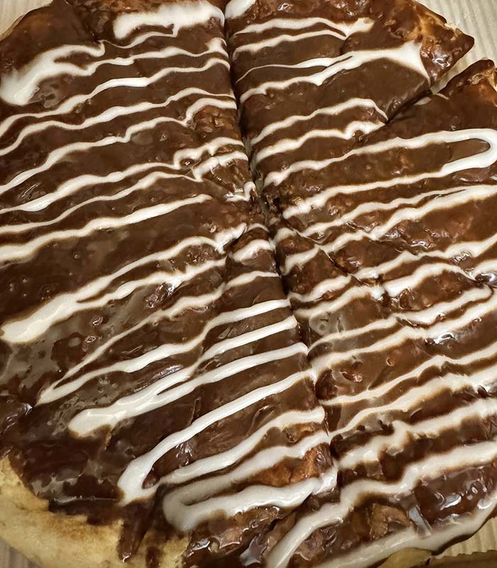 A Gatesville Pizza dessert, sliced into eight pieces, topped with a rich chocolate spread and drizzled with white icing in diagonal lines—perfect for sharing at your favorite Gatesville Restaurant.