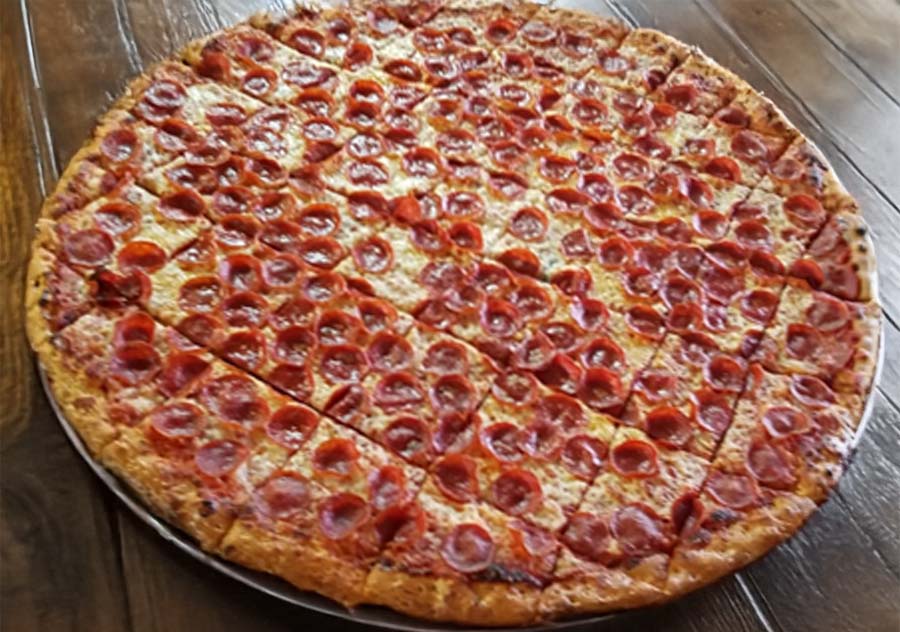 A large pepperoni pizza from Studebakers Pizza Gatesville TX is cut into many small, square pieces on a metal tray atop a wooden table. The pizza is covered evenly with pepperoni slices and melted cheese.