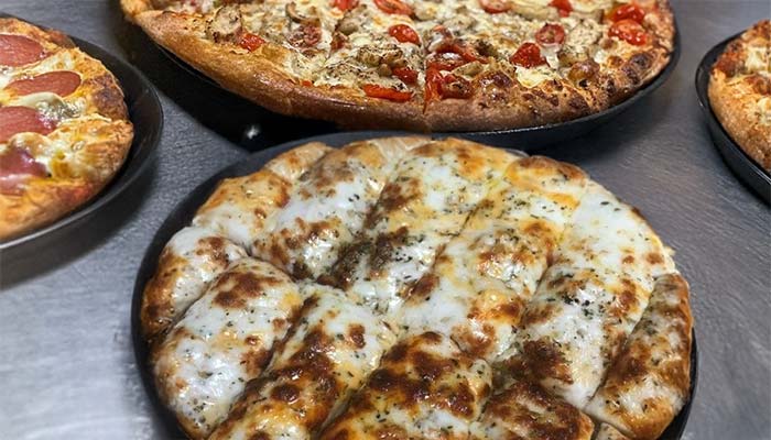 A close-up of four pizzas on a table at Pizza and Wings Gatesville TX, featuring a cheesy garlic bread pizza in front and an array of traditional pizzas with assorted toppings in the background.