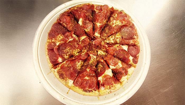 A pepperoni pizza, sliced into wedges, sits on a white plate atop a metallic surface—a classic choice you’ll find on the Studebakers Menu Gatesville TX, with some slices featuring extra seasoning or toppings in the center.