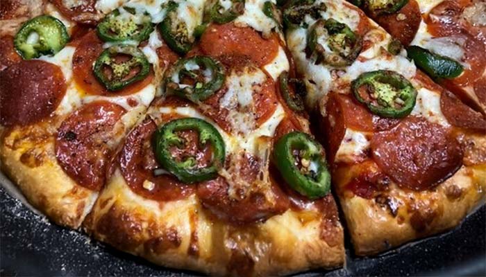 A close-up of a sliced pizza from Pizza and Wings Gatesville TX, topped with pepperoni, jalapeño slices, and melted cheese on a golden, thick crust.